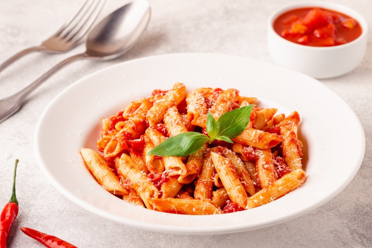 Ein Teller Penne all’arrabbiata. Daneben steht ein Schälchen mit Tomaten und es liegt Besteck links vom Teller.