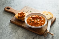 Pesto Calabrese in einer weißen Schale auf einem Holzbrett. Daneben liegt ein Stück Brot.