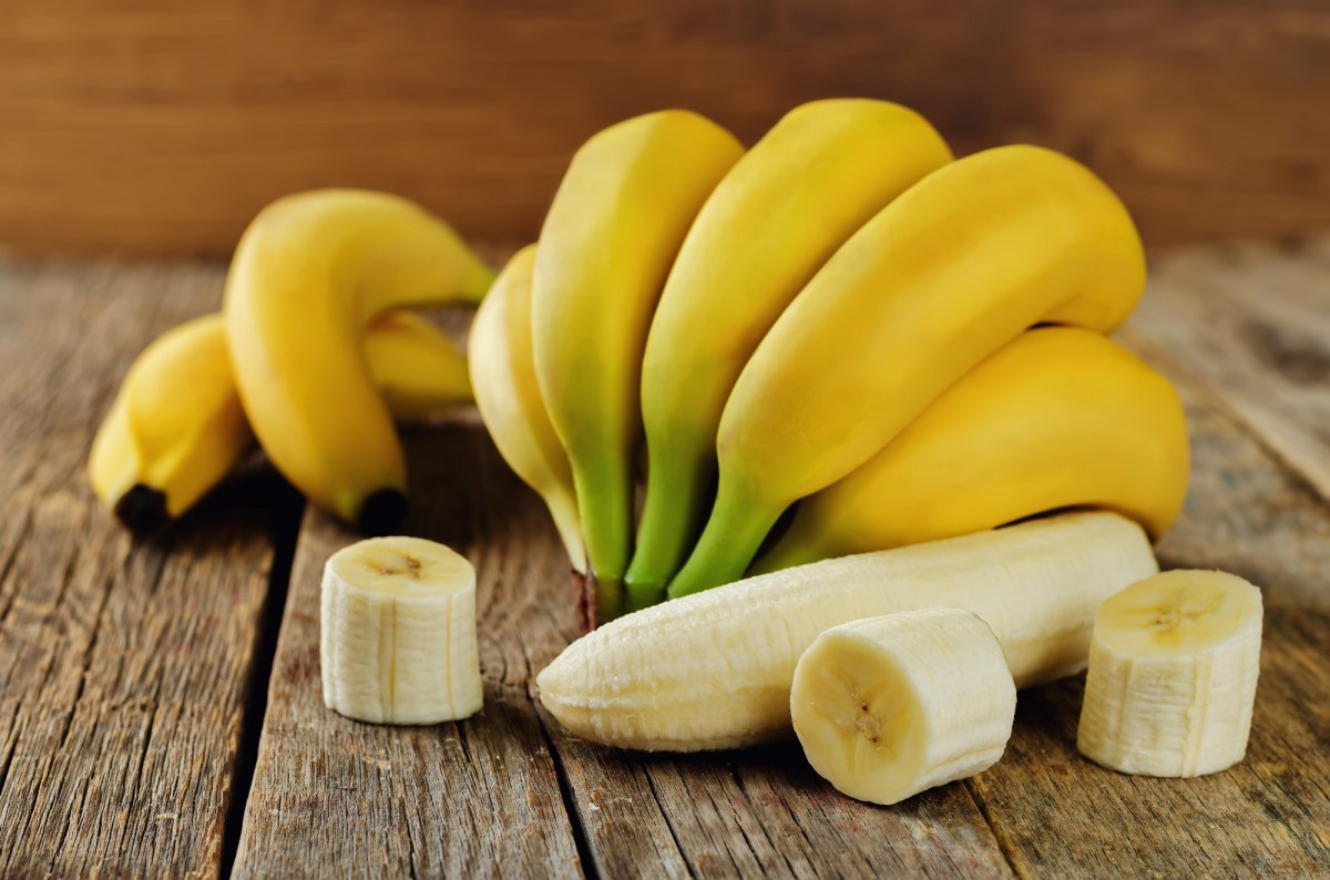 Sind Bananen gesund: Bananen mit und ohne Schale, einige geschnitten, auf Holz.