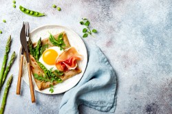 Spargel-Galette auf einem weißen Teller, garniert mit Schinken und grünem Gemüse