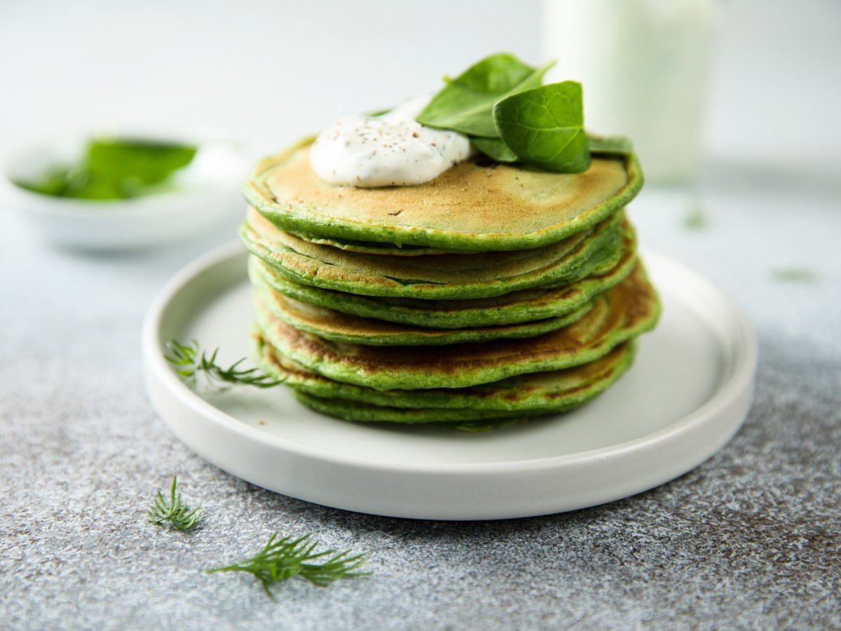 Vegane Spinat-Pancakes mit Sour Cream gestapelt auf einem Teller.