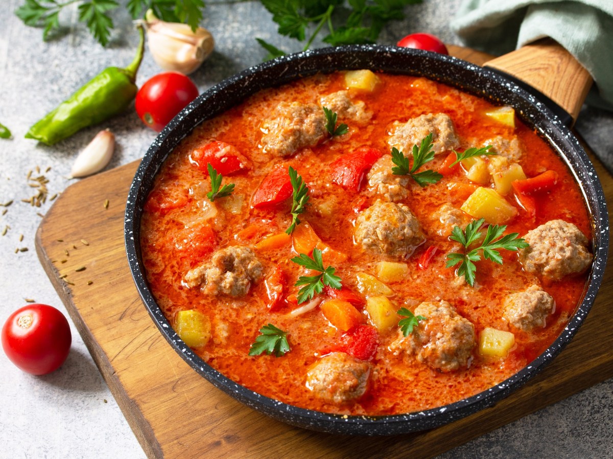 Tomatensuppe mit HackbÃ¤llchen in einer gusseisernen Pfanne, garniert mit KrÃ¤utern, daneben kleine Tomaten.