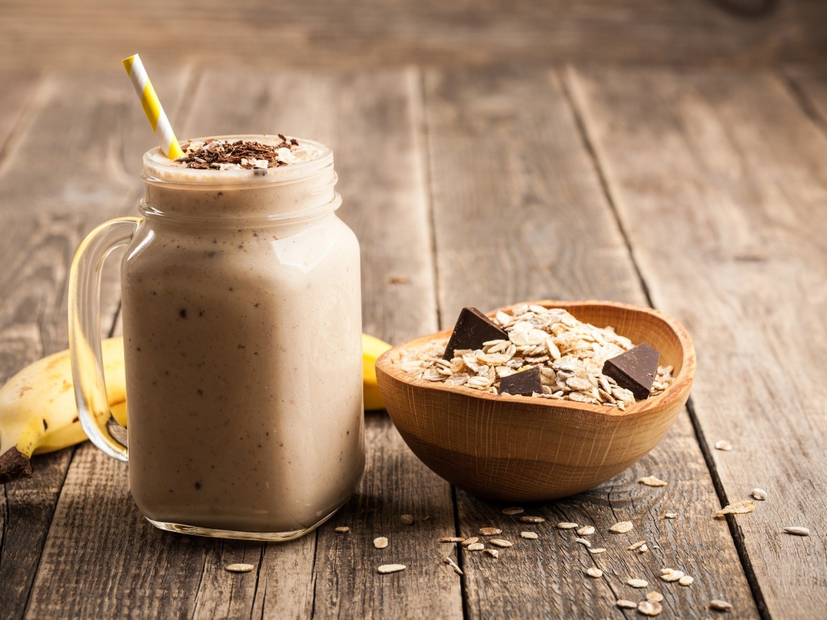 Glas mit Bananen-Schokoladen-Smoothie, Schale mit Haferflocken daneben