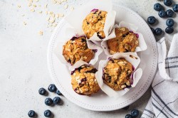 Teller mit Haferflocken-Muffins mit Blaubeeren auf hellem Untergrund