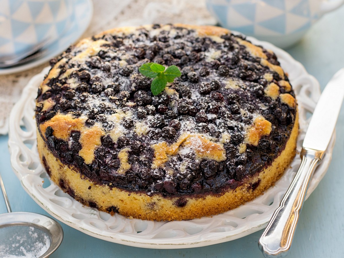 Blaubeerkuchen vom Grill auf einem runden Kuchenteller, daneben ein silbernes Messer.