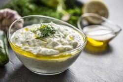 Eine Glasschüssel mit Bozner Soße, garniert mit Kräutern, im Hintergrund unscharf Zutaten und eine Schale mit Öl.