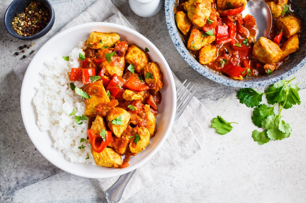 Eine Portion Chicken Jalfrezi mit Basmiatireis in einer weiÃŸen SchÃ¼ssel. Daneben eine Pfanne mit mehr von dem gericht.