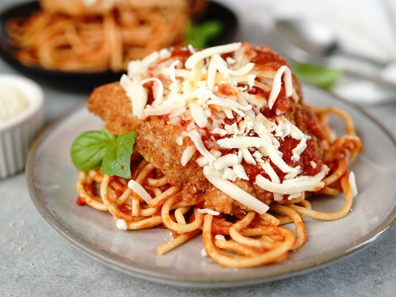 Chicken Parmesan, mit Spaghetti serviert, auf einem grauen Teller.