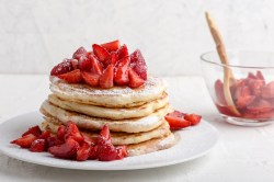 Erdbeer-Pfannkuchen auf einem weißen Teller, bestreut mit Puderzucker.