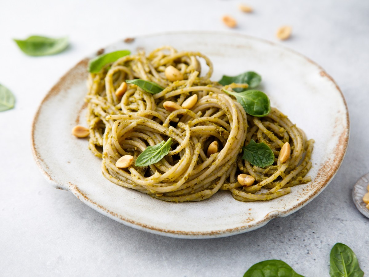 Ein Teller Spaghetti mit Erdnuss-Pesto und ErdnÃ¼ssen sowie Basilikum, Nahaufnahme.