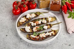 Gegrillte Aubergine mit Feta auf einem weißen Teller. Daneben liegen Kirschtomaten.