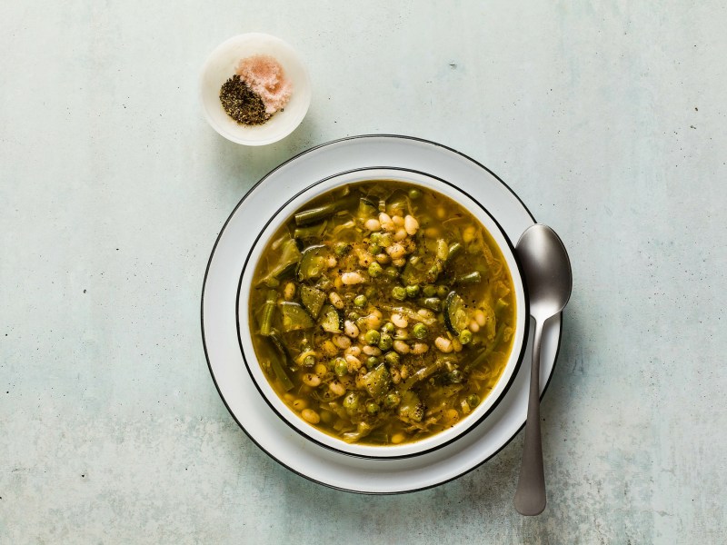 Ein Teller grüne Minestrone. Daneben steht ein Pott mit Salz und Pfeffer