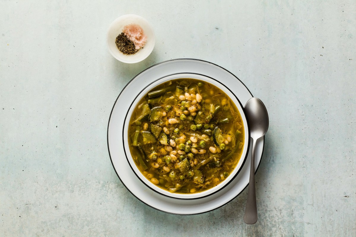 Ein Teller grüne Minestrone. Daneben steht ein Pott mit Salz und Pfeffer