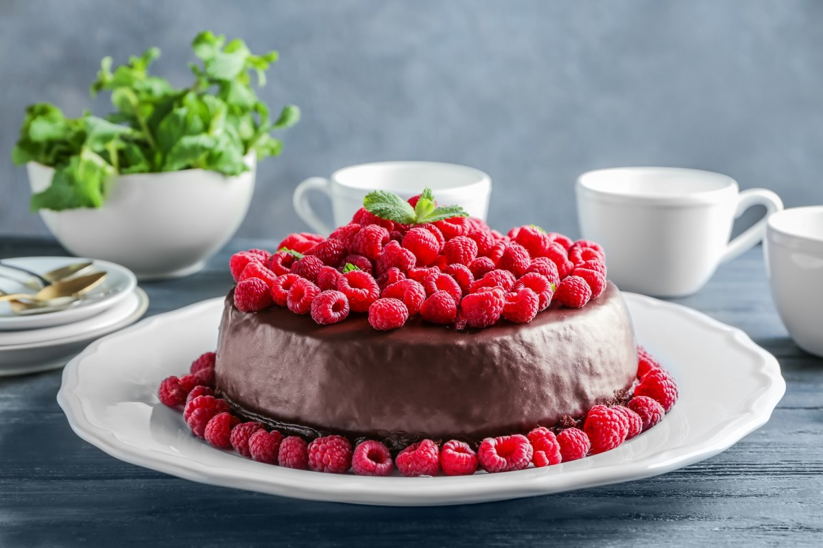 Himbeer-Schokokuchen auf einem weißen Teller. Drum herum liegen frische Himbeeren.