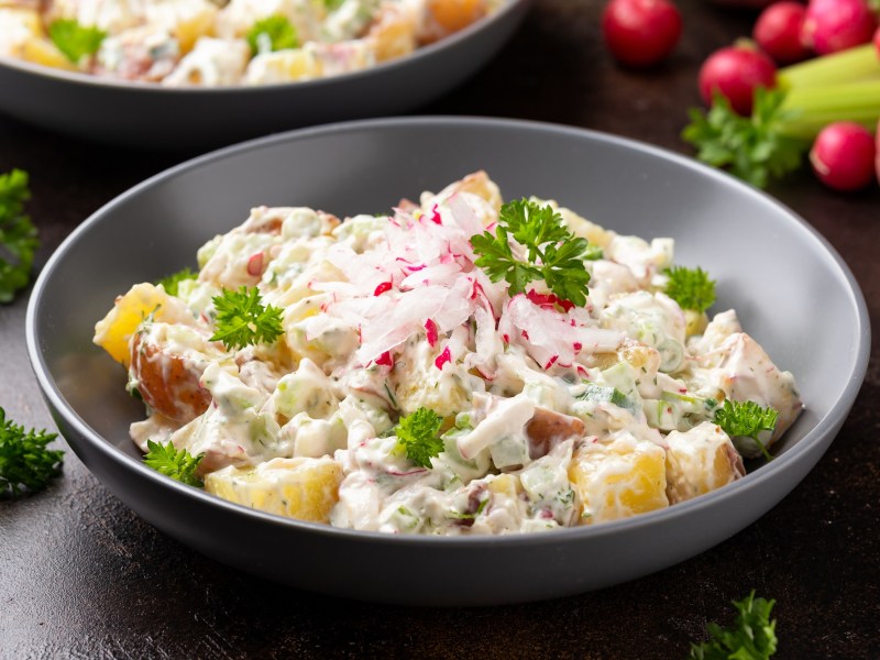 Eine Schüssel mit Kartoffelsalat mit Joghurtdressing, Radieschen und Kräutern.