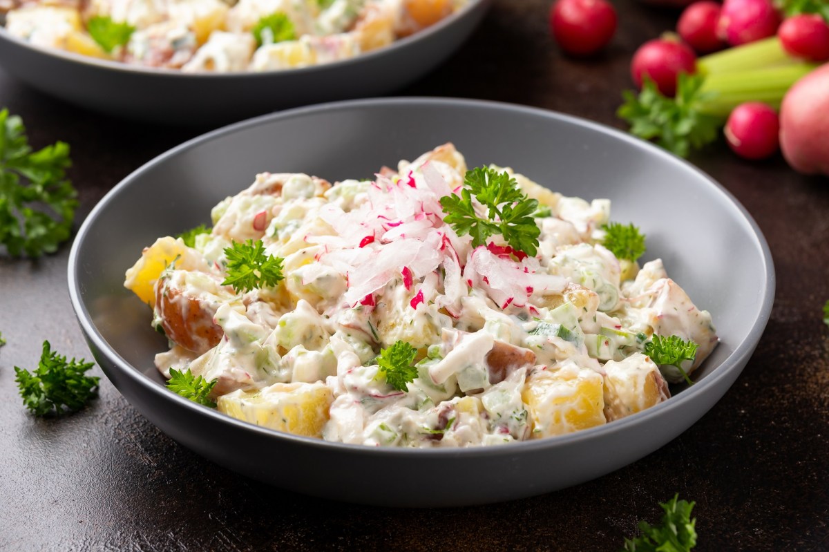 Eine Schüssel mit Kartoffelsalat mit Joghurtdressing, Radieschen und Kräutern.