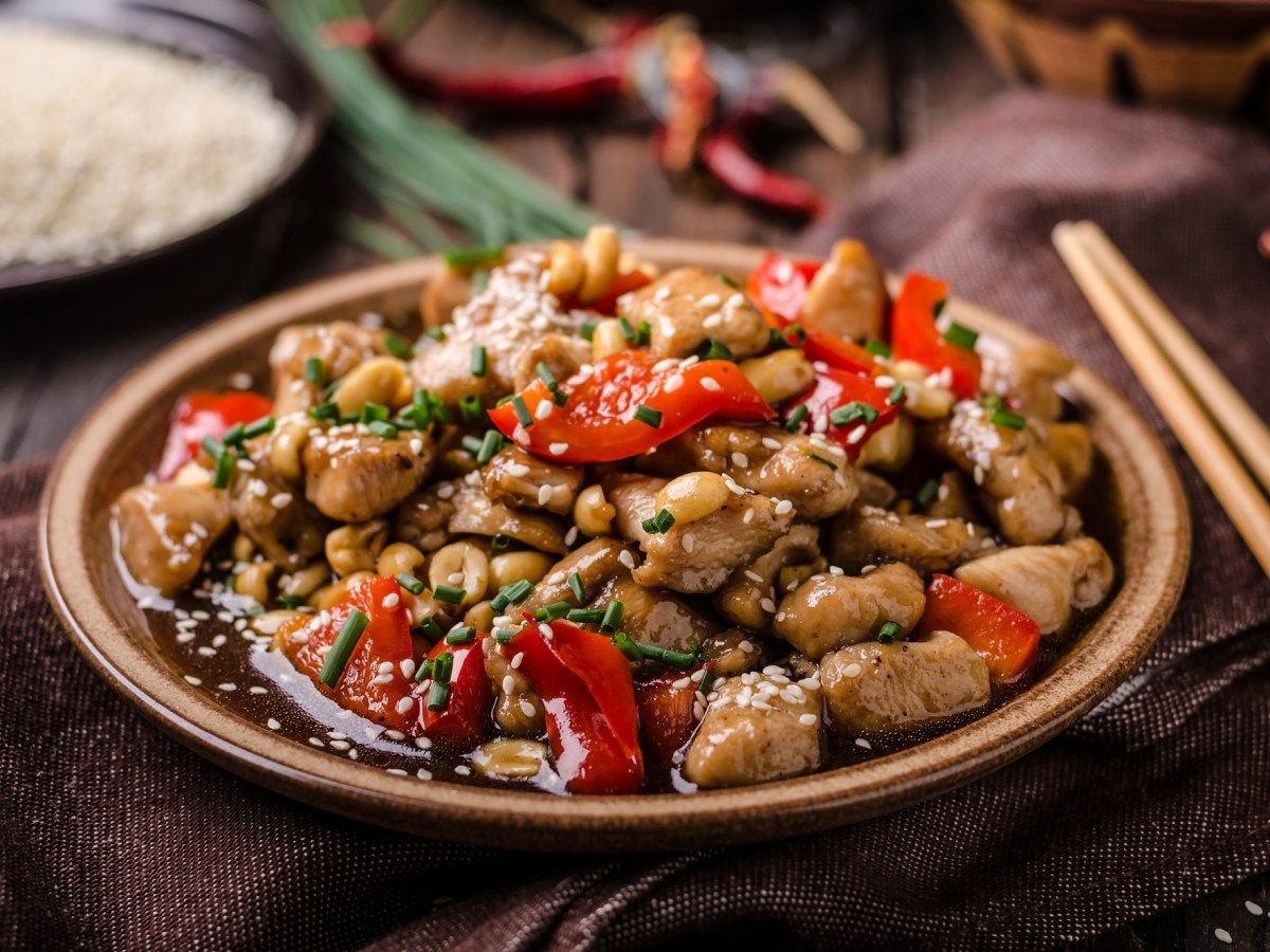 Kung Pao Chicken auf einem hellbraunen Teller. Daneben liegen Stäbchen