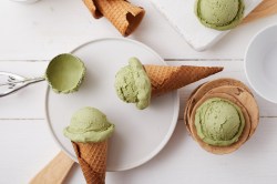 Einige Kugeln Matcha-Eis, einige in Waffeln, liegen auf einem weißen Teller.