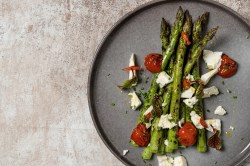 Ofenspargel mit Tomaten und Feta auf einem Teller, Draufsicht.