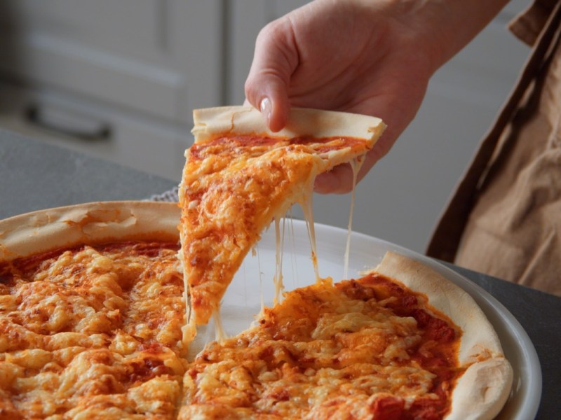Pizzateig ohne Hefe: Jemand nimmt ein Stück Pizza hoch.