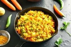 Reispfanne mit Gemüse wie Erbsen und Karotten, drumherum frische Zutaten.