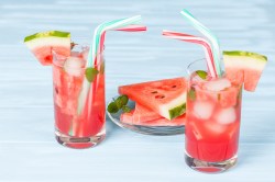 2 Gläser Sommerbowle mit Melone, Eiswürfeln und Strohhalmen, dazwischen ein Teller mit Melonenscheiben.