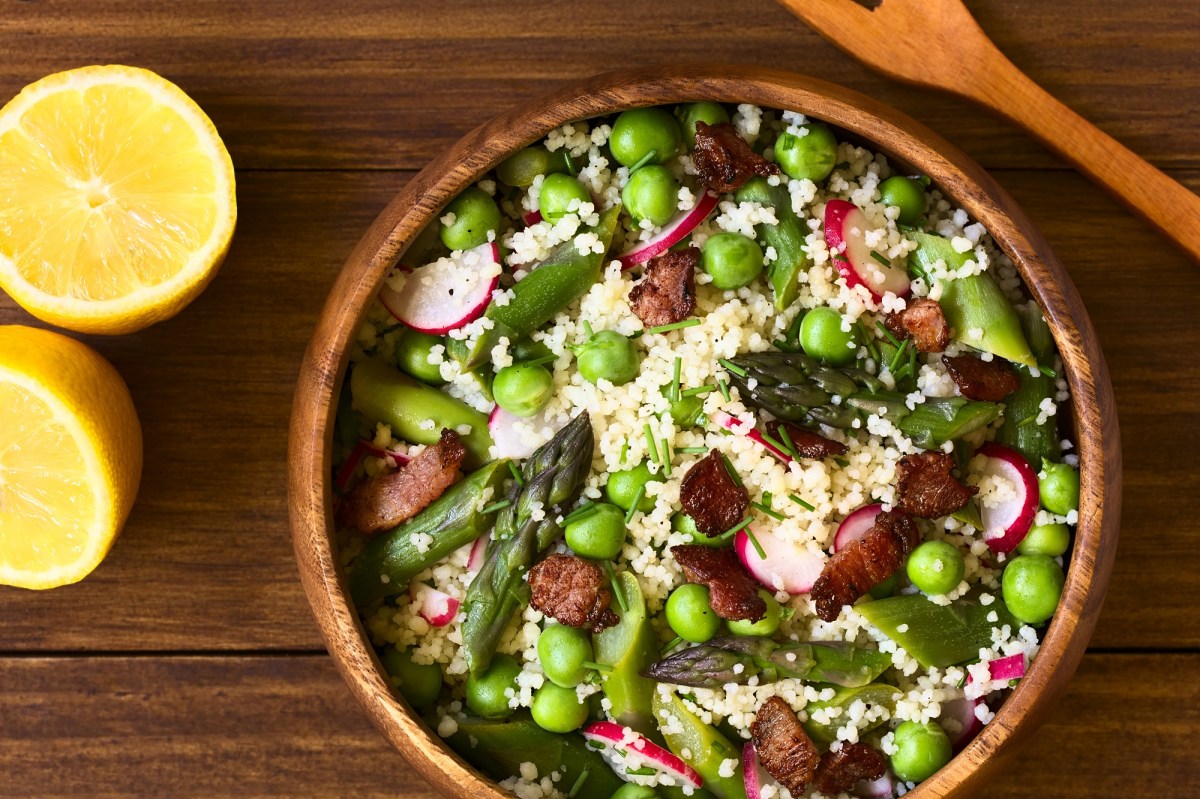 Eine HolzschÃ¼ssel (Ã–ffnet in einem neuen Browser Tab) Spargel-Couscous-Salat mit Erbsen und Radieschen in der Draufsicht, daneben eine halbierte Zitrone und ein HolzlÃ¶ffel.