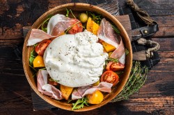 Tomatensalat mit Burrata und Schinken in einer Schüssel.