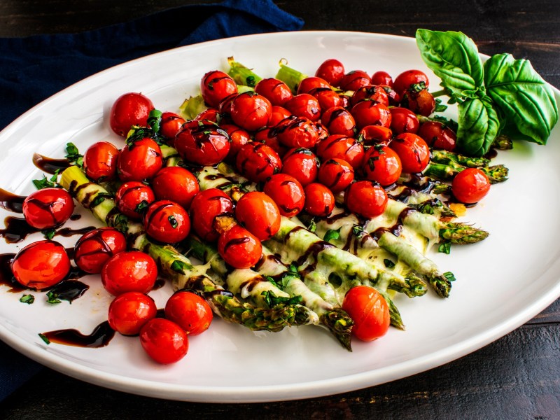 Überbackener Spargel Caprese mit Tomaten und Mozzarella, garniert mit Basilikum und Balsamico.