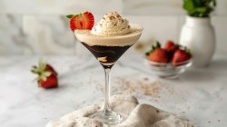 Ein Martiniglas mit Affogato Espresso Martini mit Vanilleeis und einer halben Erdbeere garniert. Im Hintergrund unscharf Erdbeeren und Zutaten.