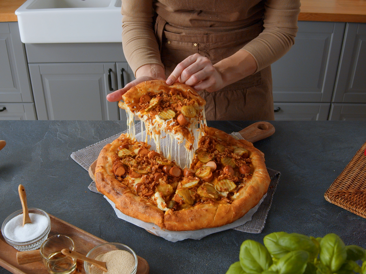 American Pizzateig: Eine Frau hebt ein Pizzastück an.