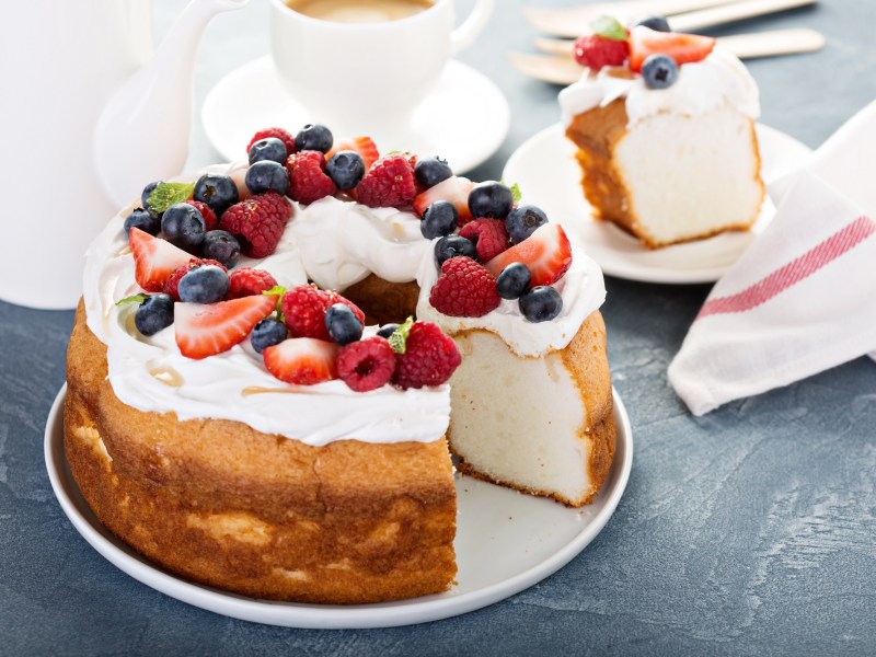 Angel Food Cake, von dem ein Stück angeschnitten wurde, auf einem weißen Teller. Der Kuchen ist garniert mit frischen Beeren.