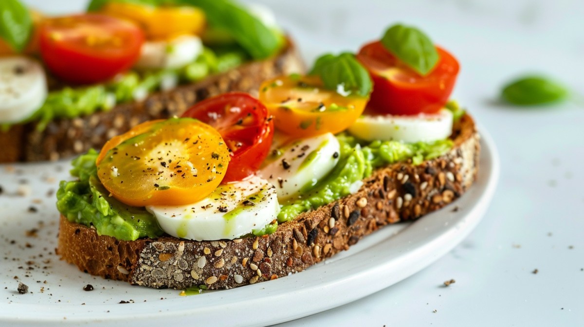 2 Avocado-Caprese-Toasts mit Tomaten und Mozzarella auf einem Teller, garniert mit Basilikum.