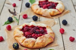 Zwei Beeren-Galettes auf einem Holztisch. Drum herum liegen frische Beeren.