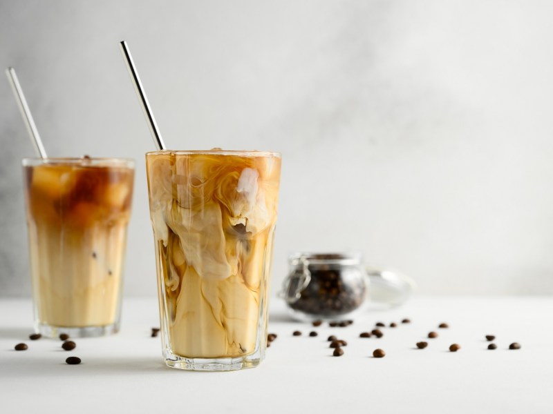 Eiskaffee selber machen: zwei Eiskaffees in Gläsern mit Trinkhalm aus Metall, daneben Kaffeebohnen.