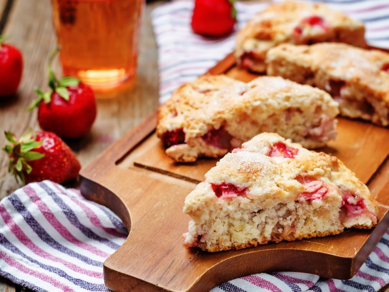 Erdbeer-Buttermilch-Scones auf einem Brett, Erdbeeren und gestreiftes Küchentuch.