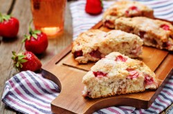 Erdbeer-Buttermilch-Scones auf einem Brett, Erdbeeren und gestreiftes Küchentuch.
