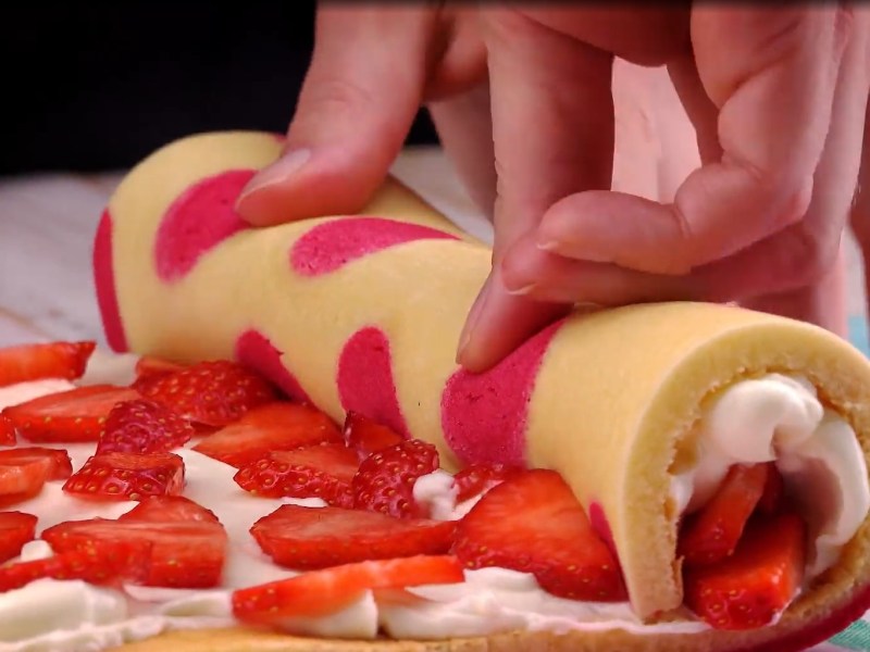 Eine Erdbeer-Käsekuchen-Rolle wird aufgerollt