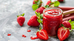 Ein Glas Erdbeer-Rhabarber-Marmelade. Daneben Erdbeeren und Rhabarberstangen.