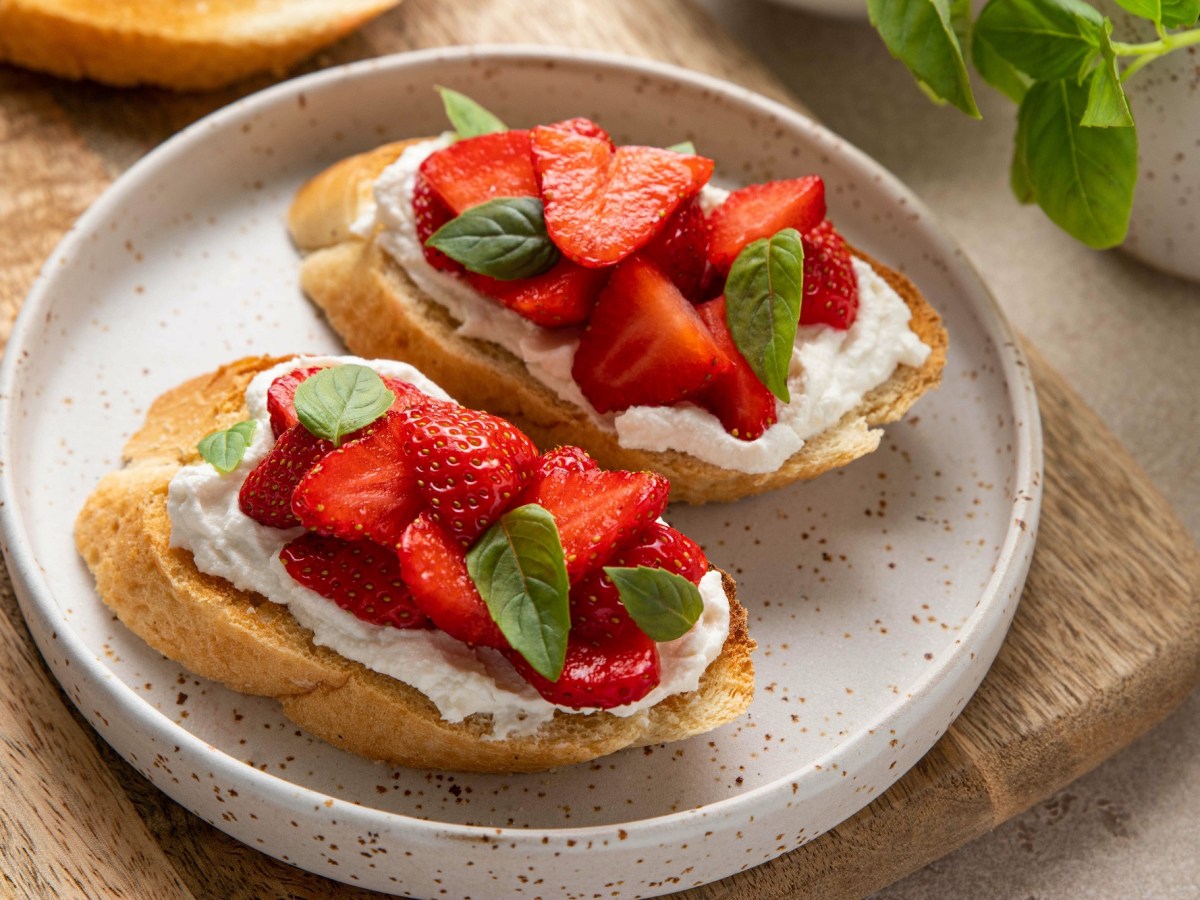 Zwei Erdbeer-Ricotta-Crostini auf einem weißen Teller. Garniert sind sie mit Basilikum.