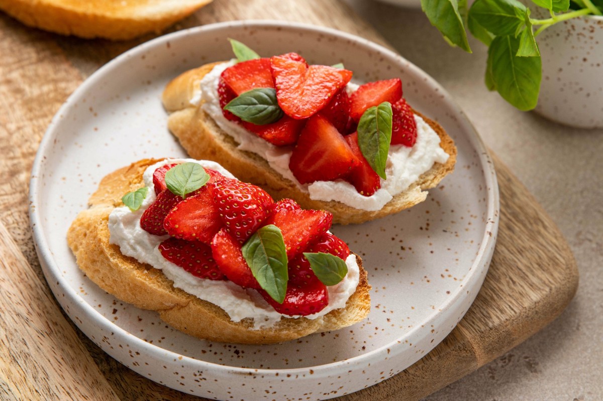 Zwei Erdbeer-Ricotta-Crostini auf einem weißen Teller. Garniert sind sie mit Basilikum.