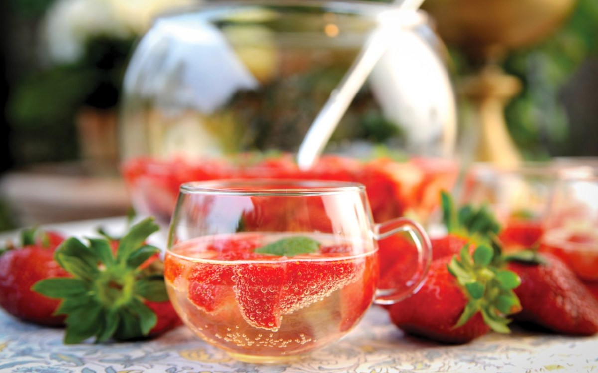 Ein Glas Erdbeerbowle vor einem Bowletopf.