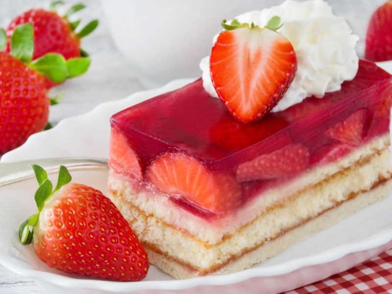 Eine Erdbeerschnitte auf einem Teller, dekoriert mit frischen Erdbeeren und Sahne.