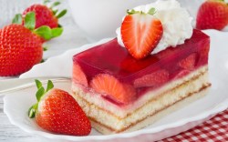 Eine Erdbeerschnitte auf einem Teller, dekoriert mit frischen Erdbeeren und Sahne.