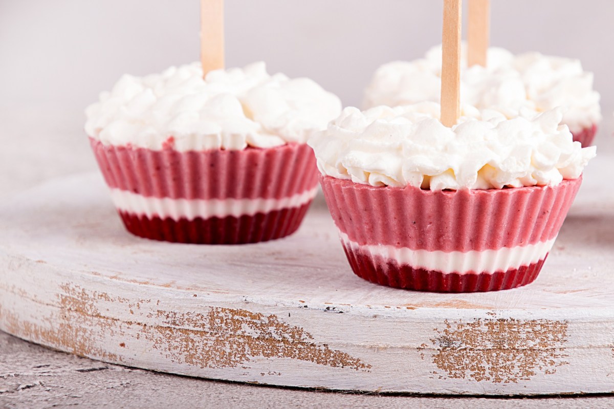 3 Frozen-Yogurt-Muffins garniert mit Sahnetupfen auf einem Brett.