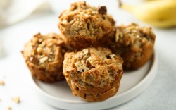 Vier Frühstücksmuffins mit Haferflocken und Nüssen auf einem Teller.