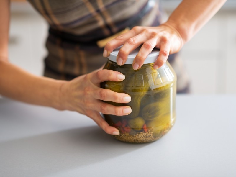 Gurkenwasser verwenden: Eine Frau öffnet ein Glas mit Gewürzgurken, man sieht nur ihre Hände.