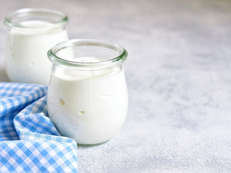 Joghurt selber machen: zwei Gläser Joghurtauf einer grauen Oberfläche. Daneben ein kariertes Tuch.