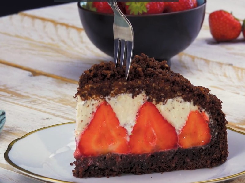 ein Stück Maulwurfkuchen mit Erdbeeren auf einem Teller, darin steckt eine Gabel.