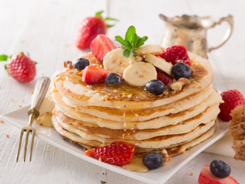 Ein Stapel Pancakes ohne Ei, mit Beeren, Nüssen und Ahornsirup.